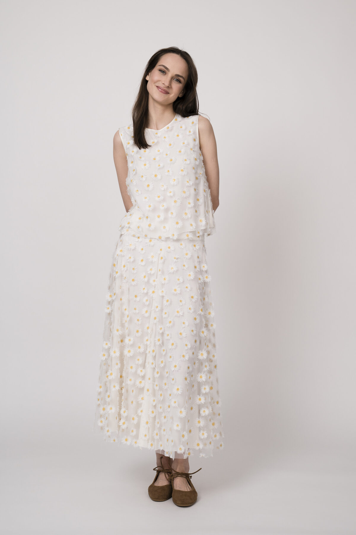 Model trägt ein weißes Top und einen weißes Rock mit Tüll und Gänseblümchen-Applikationen der Marke Luisa Cerano.