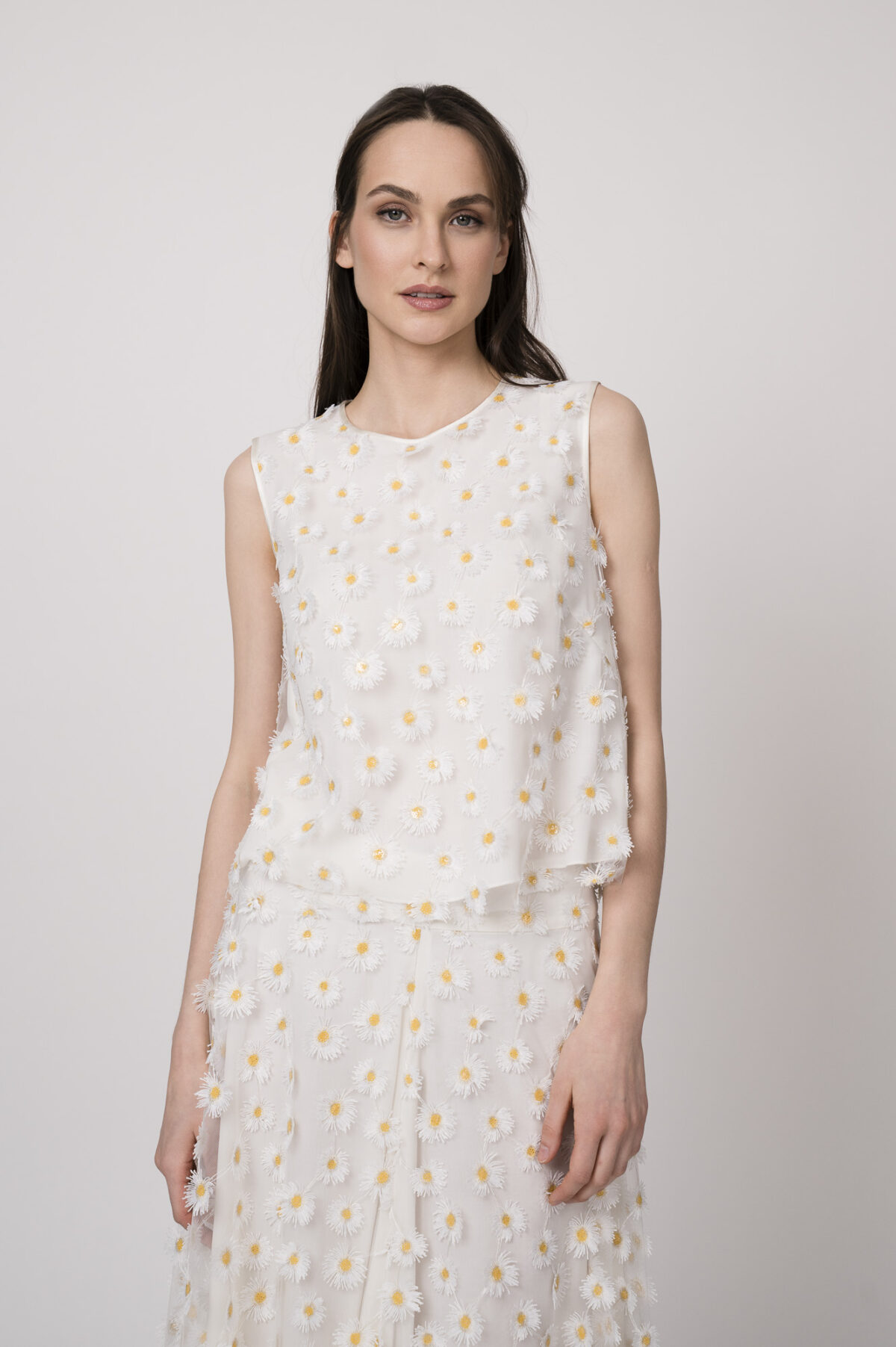 Model trägt ein weißes Top mit Tüll und Gänseblümchen-Applikationen der Marke Luisa Cerano.