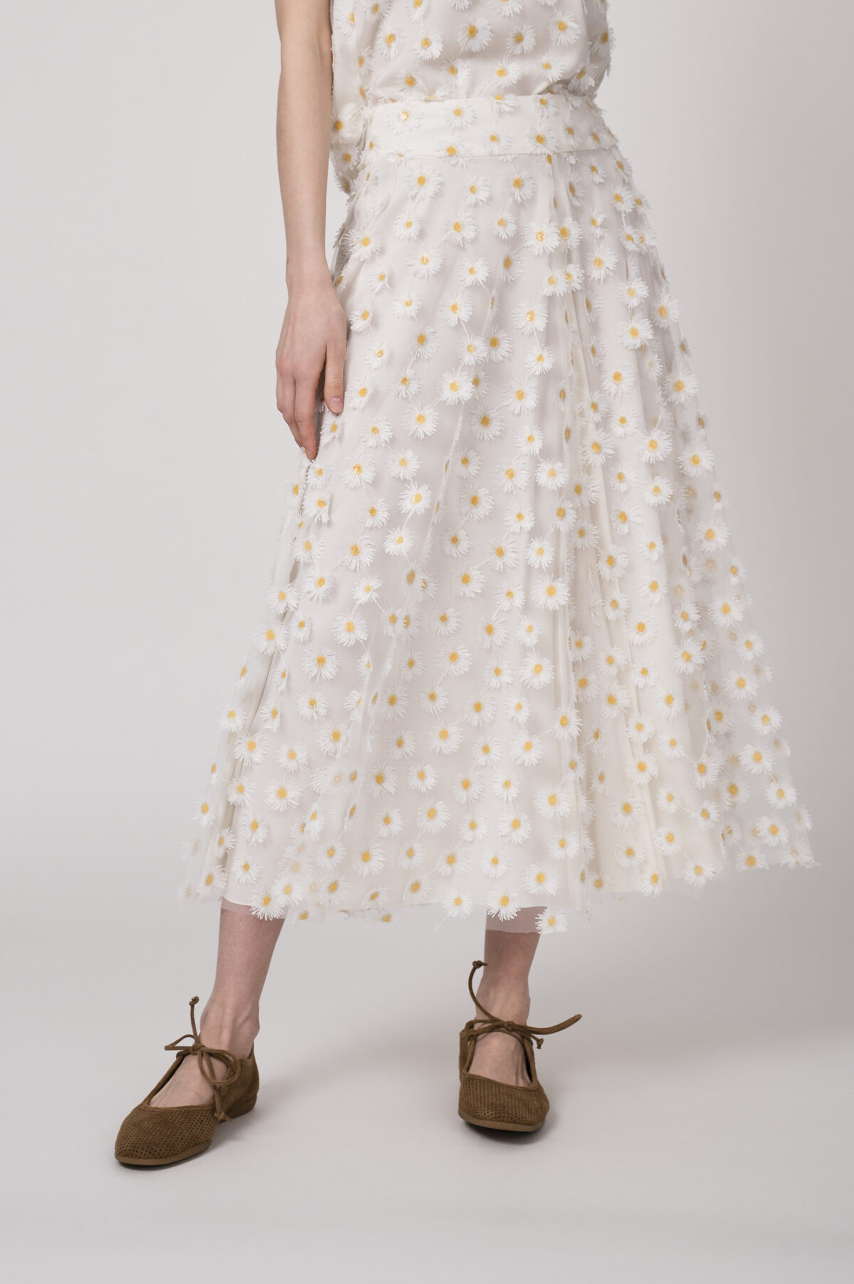 Model trägt einen weißen Rock mit Tüll und Gänseblümchen-Applikationen der Marke Luisa Cerano.
