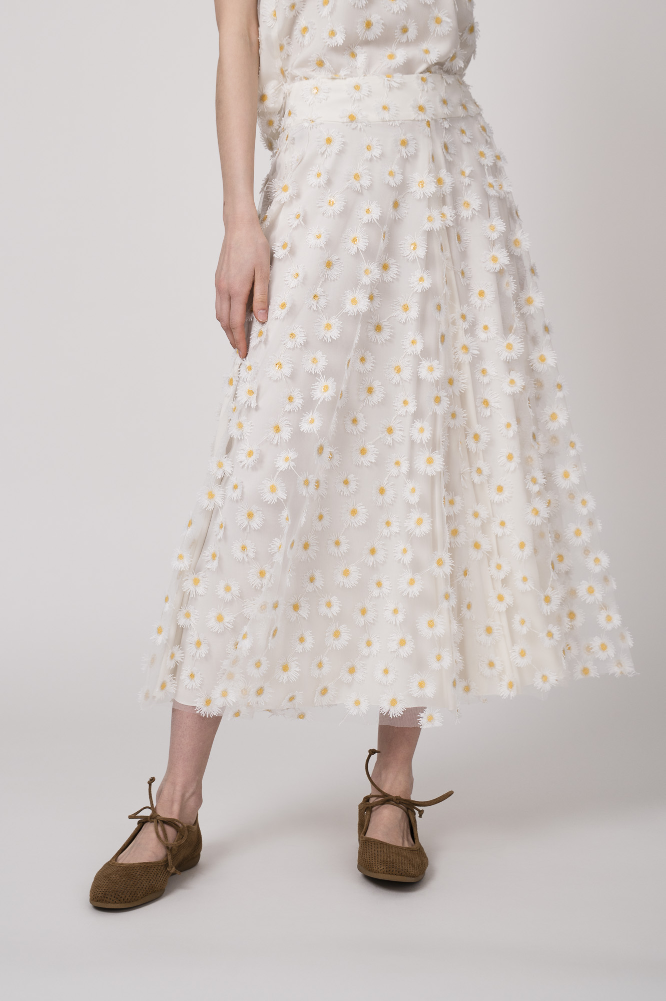 Model trägt einen weißen Rock mit Tüll und Gänseblümchen-Applikationen der Marke Luisa Cerano.