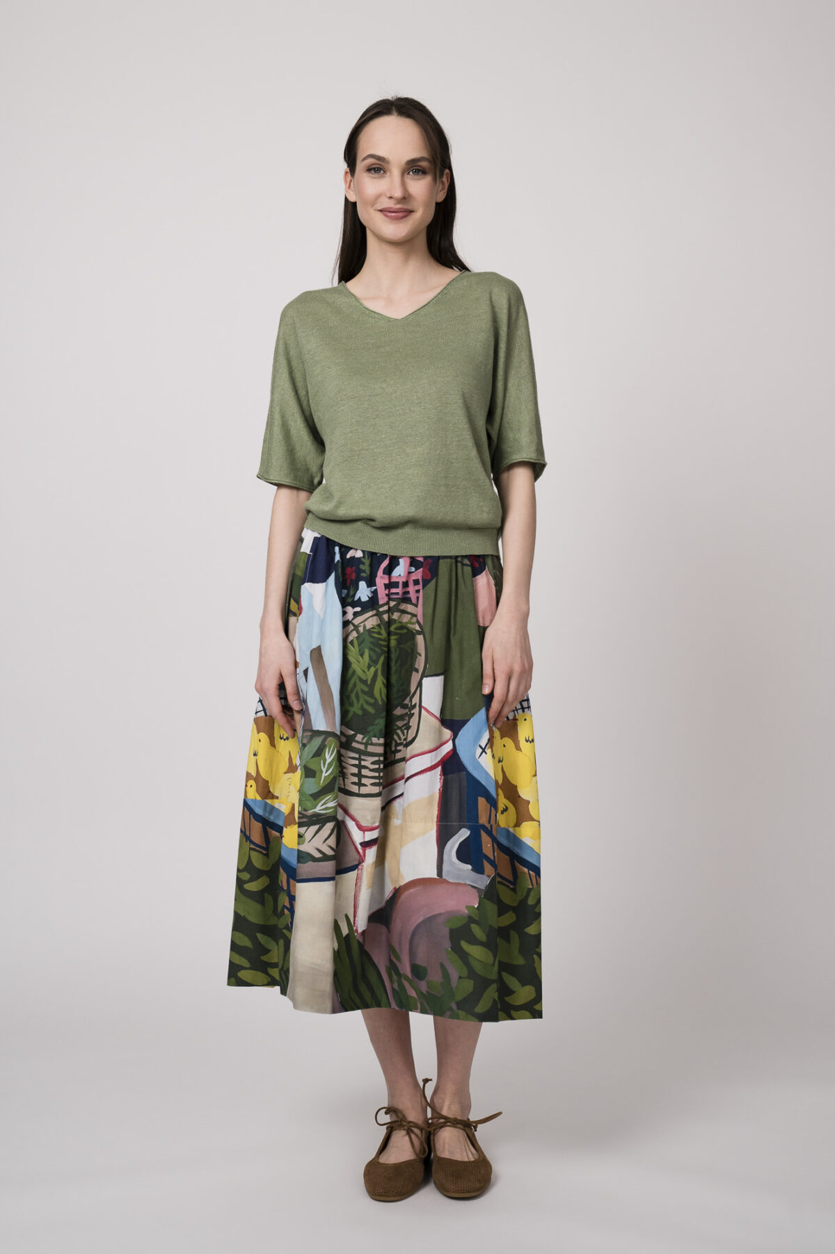 Model trägt einen grünen Kurzarmpullover der Marke Luisa Cerano und einen Rock mit buntem Print der Marke Talking Walls.