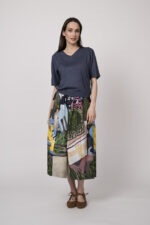 Model trägt einen blauen Kurzarmpullover der Marke Luisa Cerano und einen Rock mit buntem Print der Marke Talking Walls.