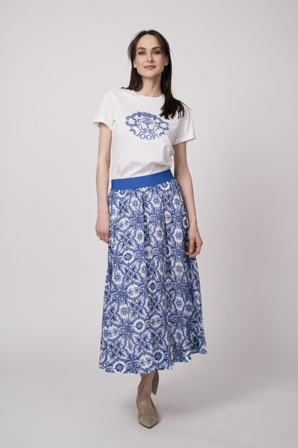 Model trägt ein weißes Shirt mit Logoprint und einen blau-weiß gemusterten Rock der Marke Joop!