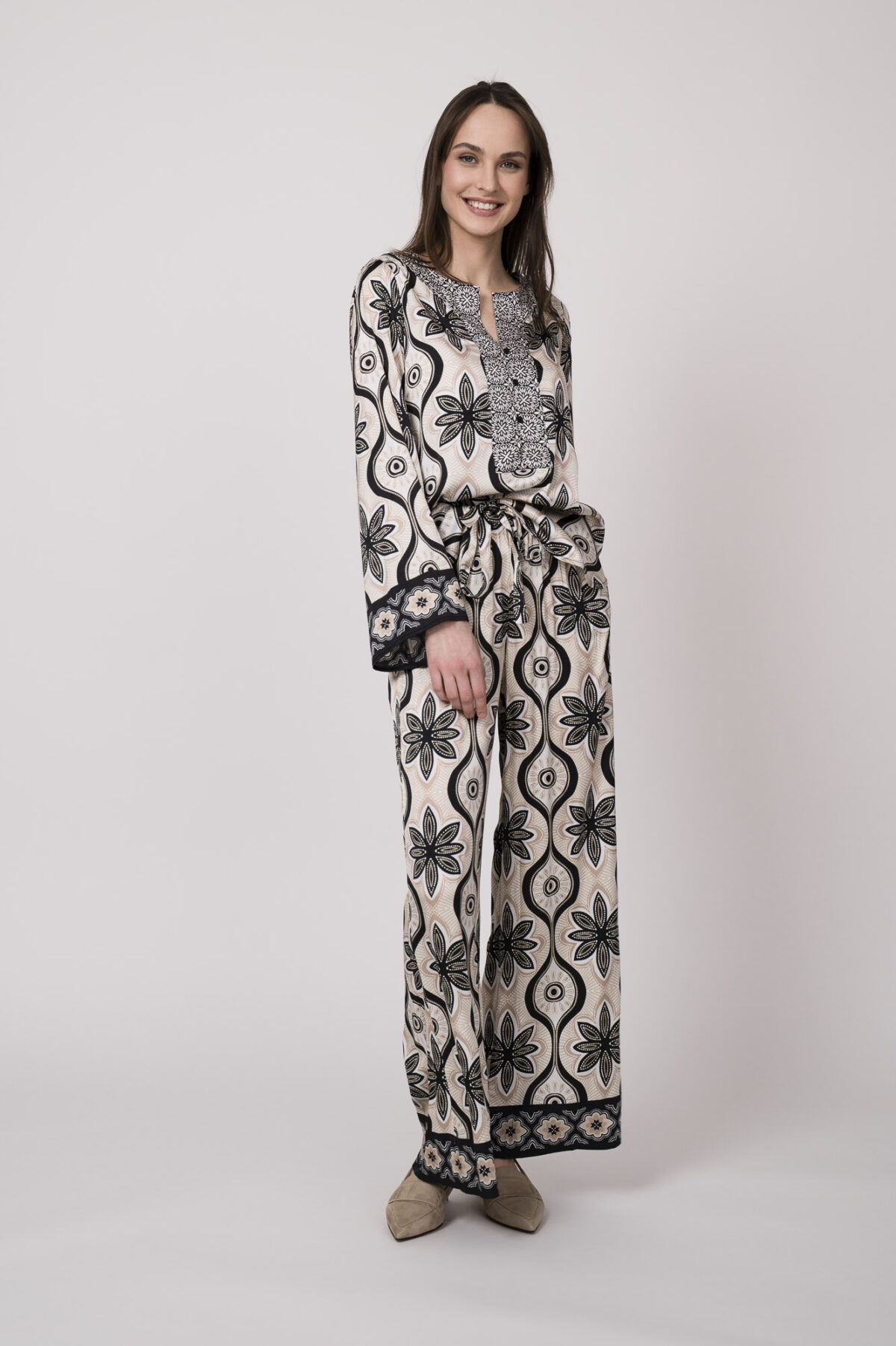 Model trägt eine grün, schwarz und beige gemusterte Bluse und Hose der Marke Grace.