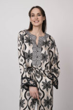 Model trägt eine grün, schwarz und beige gemusterte Bluse der Marke Grace.