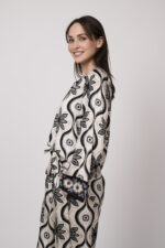 Model trägt eine grün, schwarz und beige gemusterte Bluse der Marke Grace.