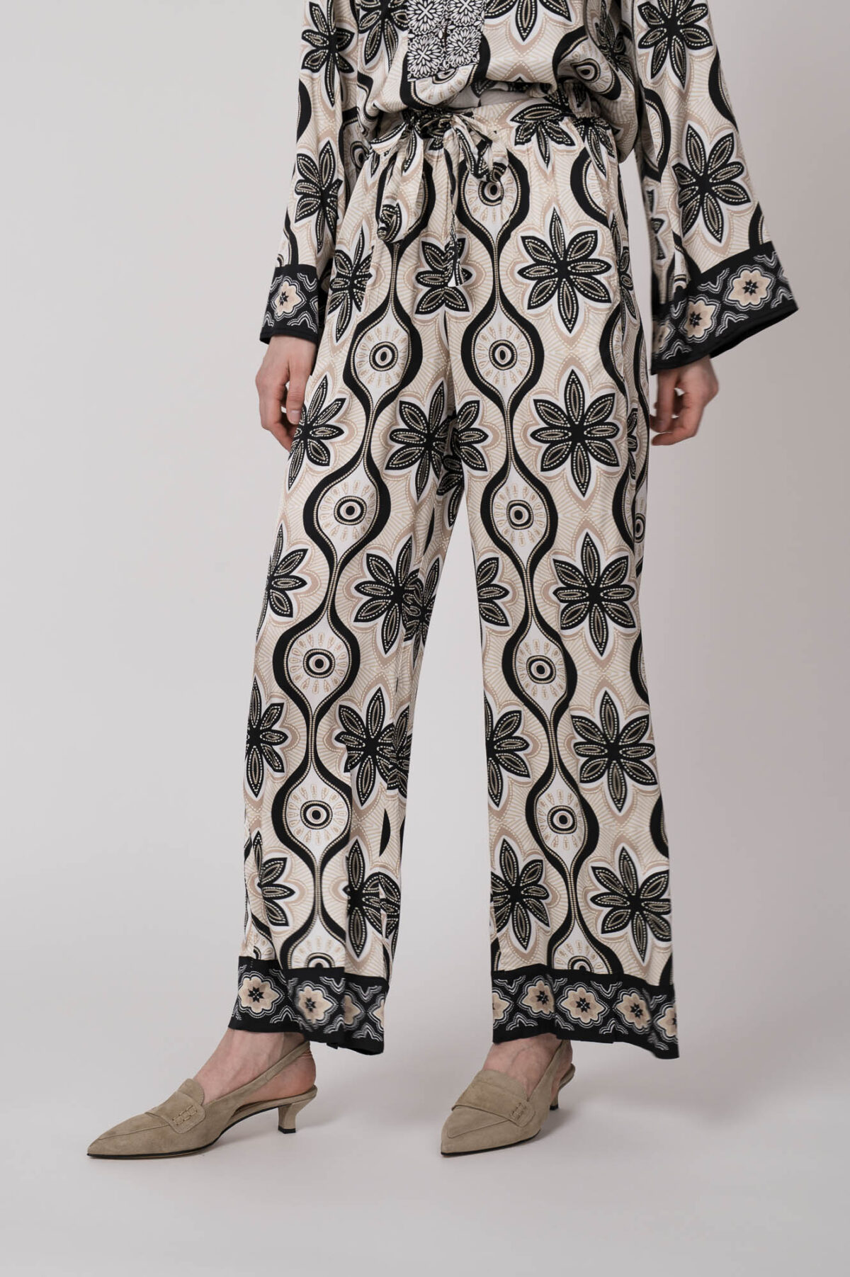 Model trägt eine grün, schwarz und beige gemusterte Hose der Marke Grace.