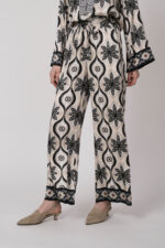 Model trägt eine grün, schwarz und beige gemusterte Hose der Marke Grace.