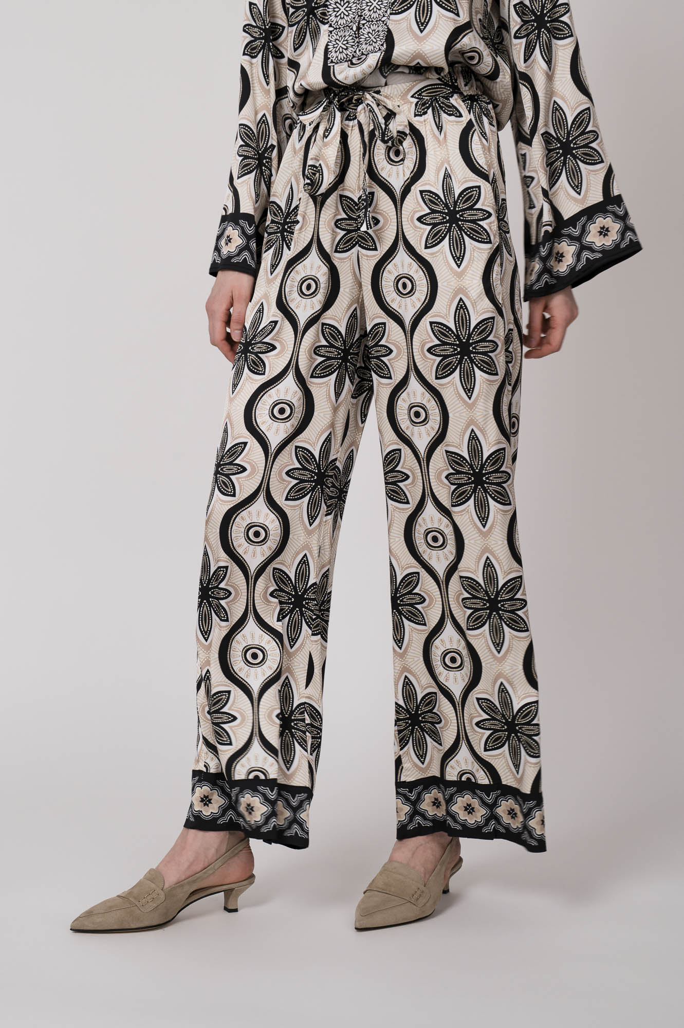 Model trägt eine grün, schwarz und beige gemusterte Hose der Marke Grace.