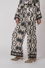 Model trägt eine grün, schwarz und beige gemusterte Hose der Marke Grace.