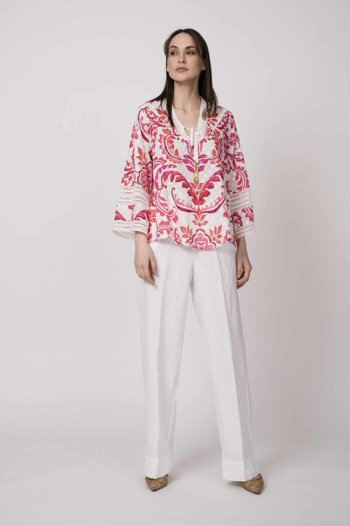 Model trägt eine Tunika mit weiß-rotem Printmuster der Marke Grace und eine weiße Hose der Marke Masons‘.