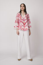 Model trägt eine Tunika mit weiß-rotem Printmuster der Marke Grace und eine weiße Hose der Marke Masons‘.