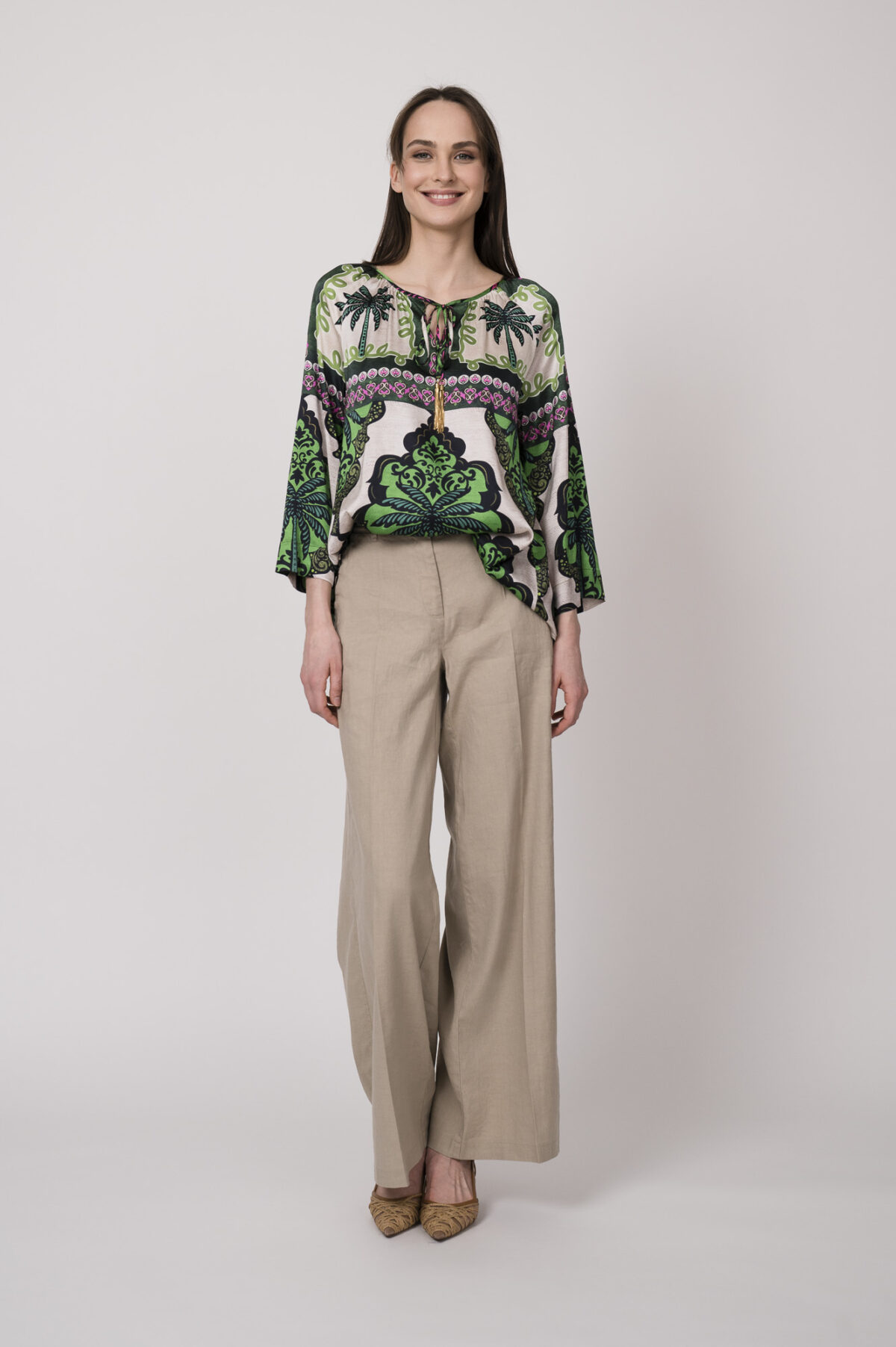 Model trägt eine grün, weiß und pink gemusterte Bluse der Marke Grace und eine beige Hose der Marke Cambio.
