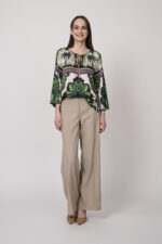 Model trägt eine grün, weiß und pink gemusterte Bluse der Marke Grace und eine beige Hose der Marke Cambio.