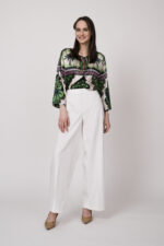 Model trägt eine grün, weiß und pink gemusterte Bluse der Marke Grace und eine weiße Hose der Marke Cambio.