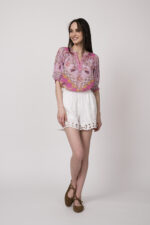 Model trägt eine pinke Bluse mit Print der Marke Hale Bob und eine weiße Shorts mit Cutouts der Marke 0039Italy.