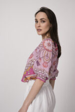 Model trägt eine pinke Bluse mit Print der Marke Hale Bob und eine weiße Shorts mit Cutouts der Marke 0039Italy.