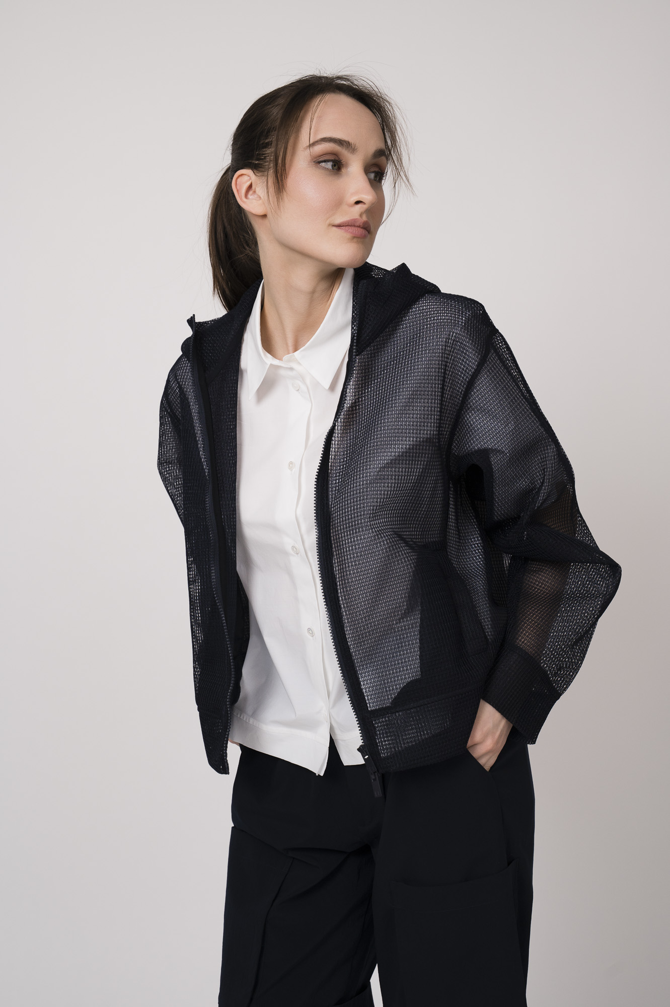Model trägt eine marine-blaue Netzjacke mit Kapuze und eine weiße Kurzarmbluse der Marke Lis Lareida.