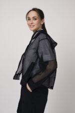 Model trägt eine marine-blaue Netzjacke mit Kapuze und eine weiße Kurzarmbluse der Marke Lis Lareida.