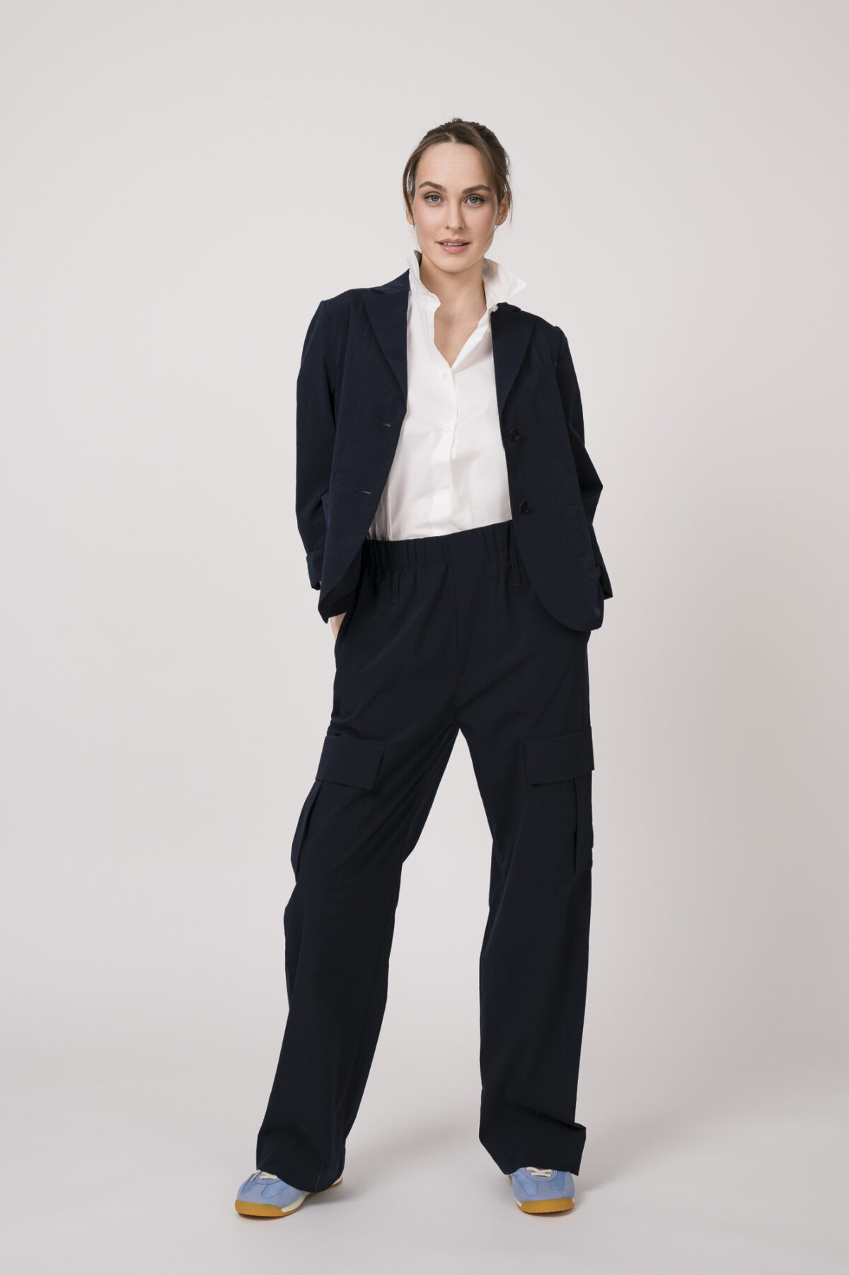Model trägt einen marine-blauen Blazer, eine marine-blaue Hose mit Seitentaschen und eine weiße Bluse der Marke Lis Lareida.