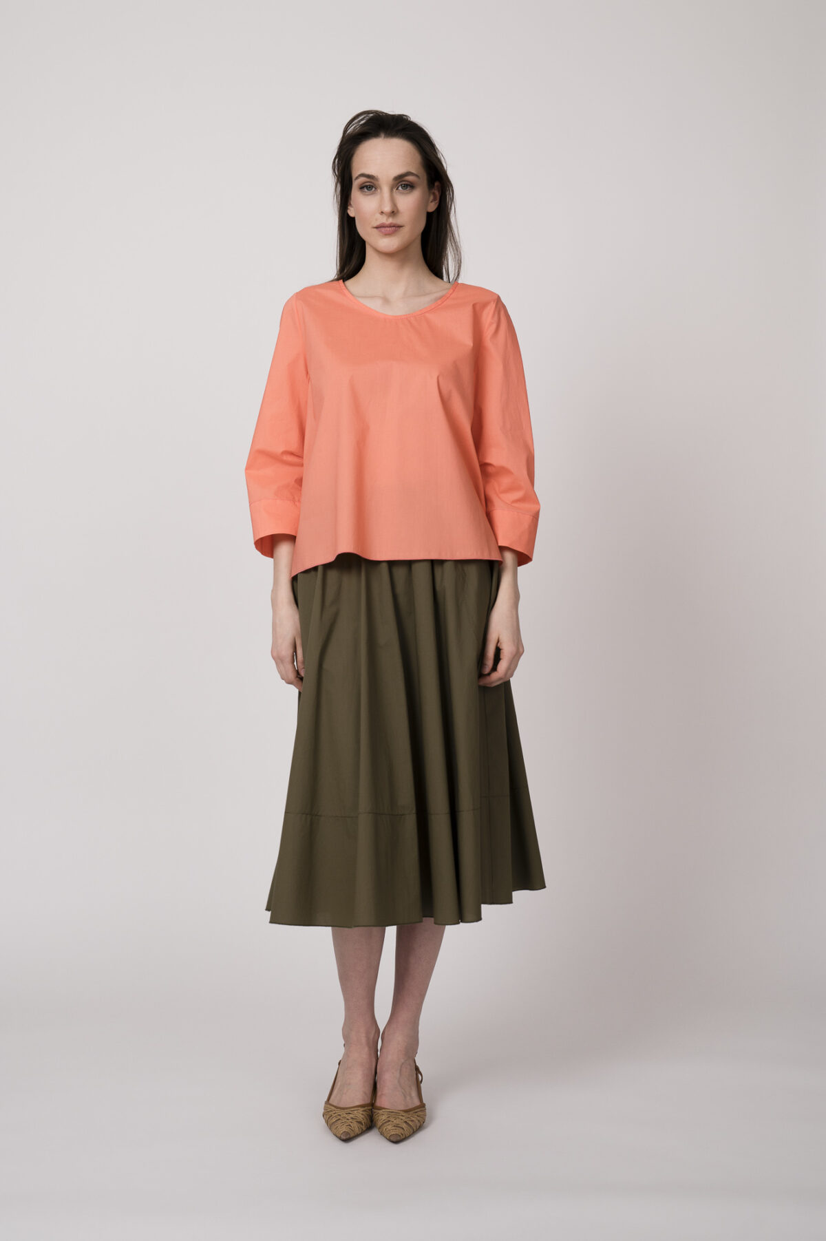 Model trägt eine orange Bluse und einen olivgrünen Rock der Marke Susanne Bommer.