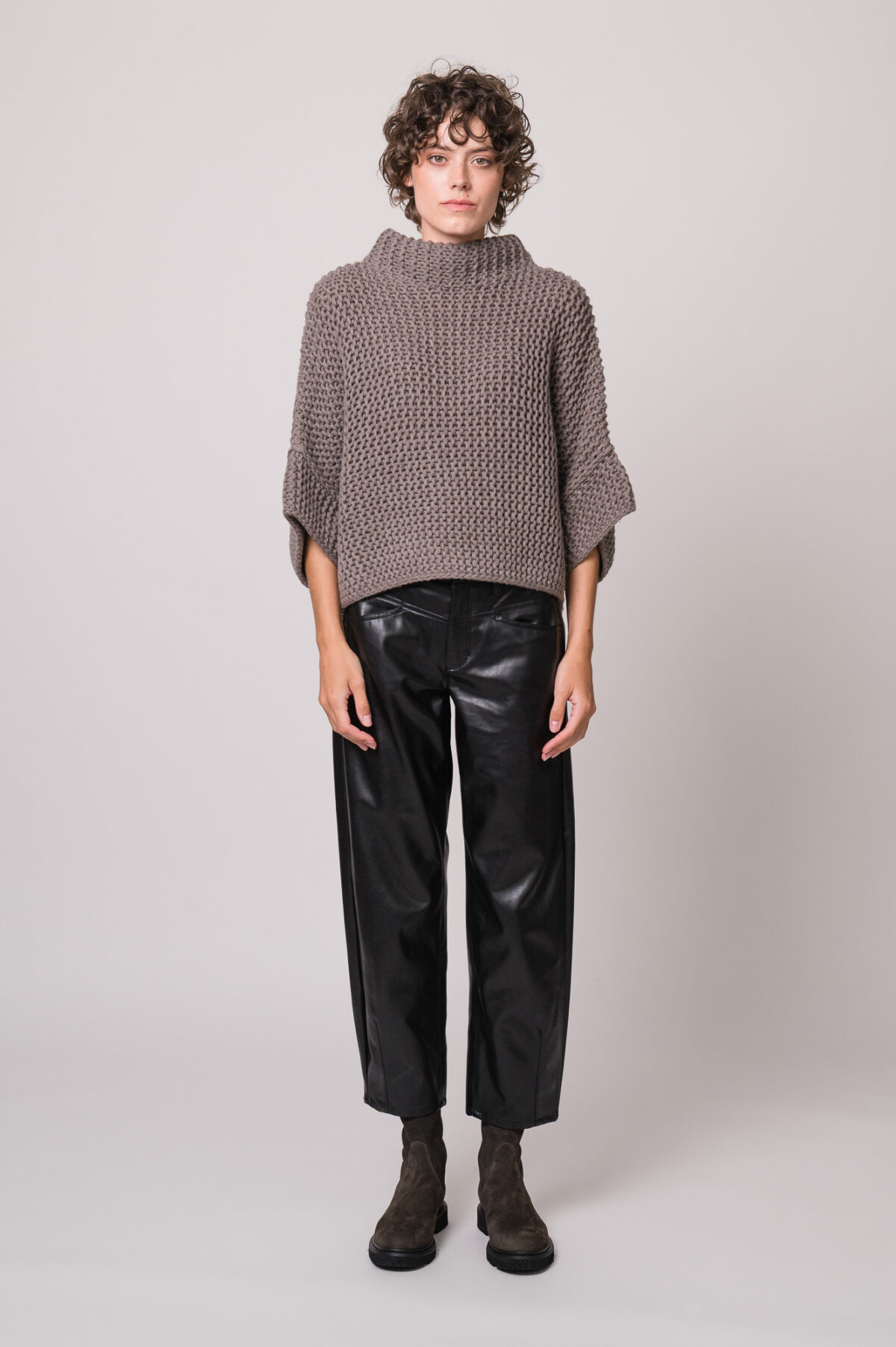 Model trägt einen grauen Kurzarm-Strickpullover der Marke FFC und eine schwarze Fake Lederhose der Marke Cambio.
