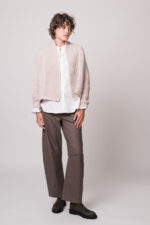 Model trägt eine weiße Bluse der Marke Rossana Diva, eine beige Strickjacke der Marke FFC und eine brauen Stoffhose der Marke Cambio.
