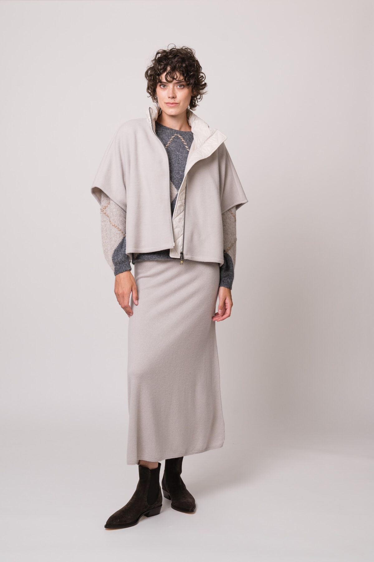 Model trägt ein hellgraues Cape, einen grau gemusterten Pullover und einen hellgrauen Rock der Marke Luisa Cerano.