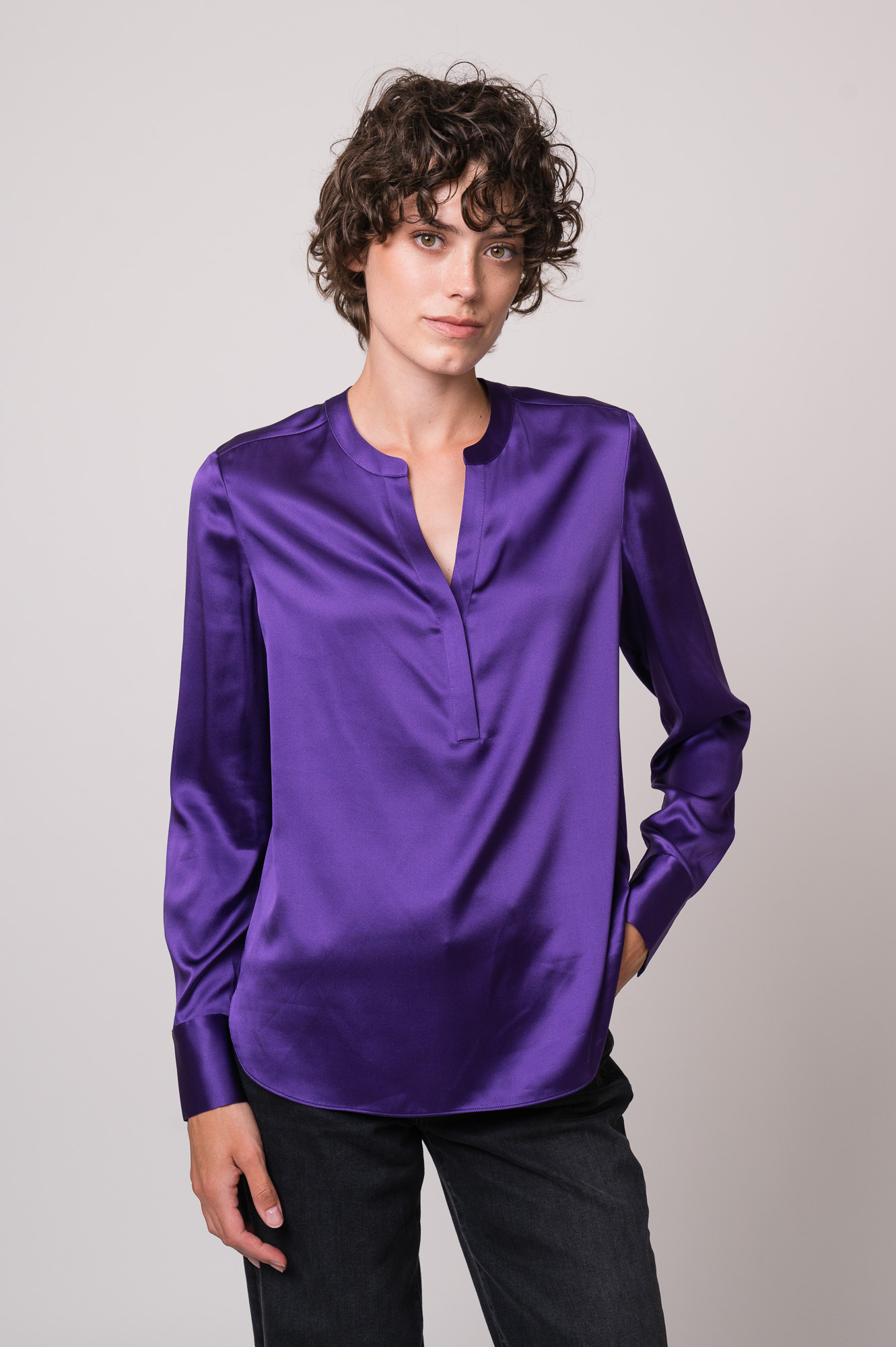 Model trägt eine violette Bluse der Marke Herzens und eine schwarze Jeans der Marke 7 for all mankind.