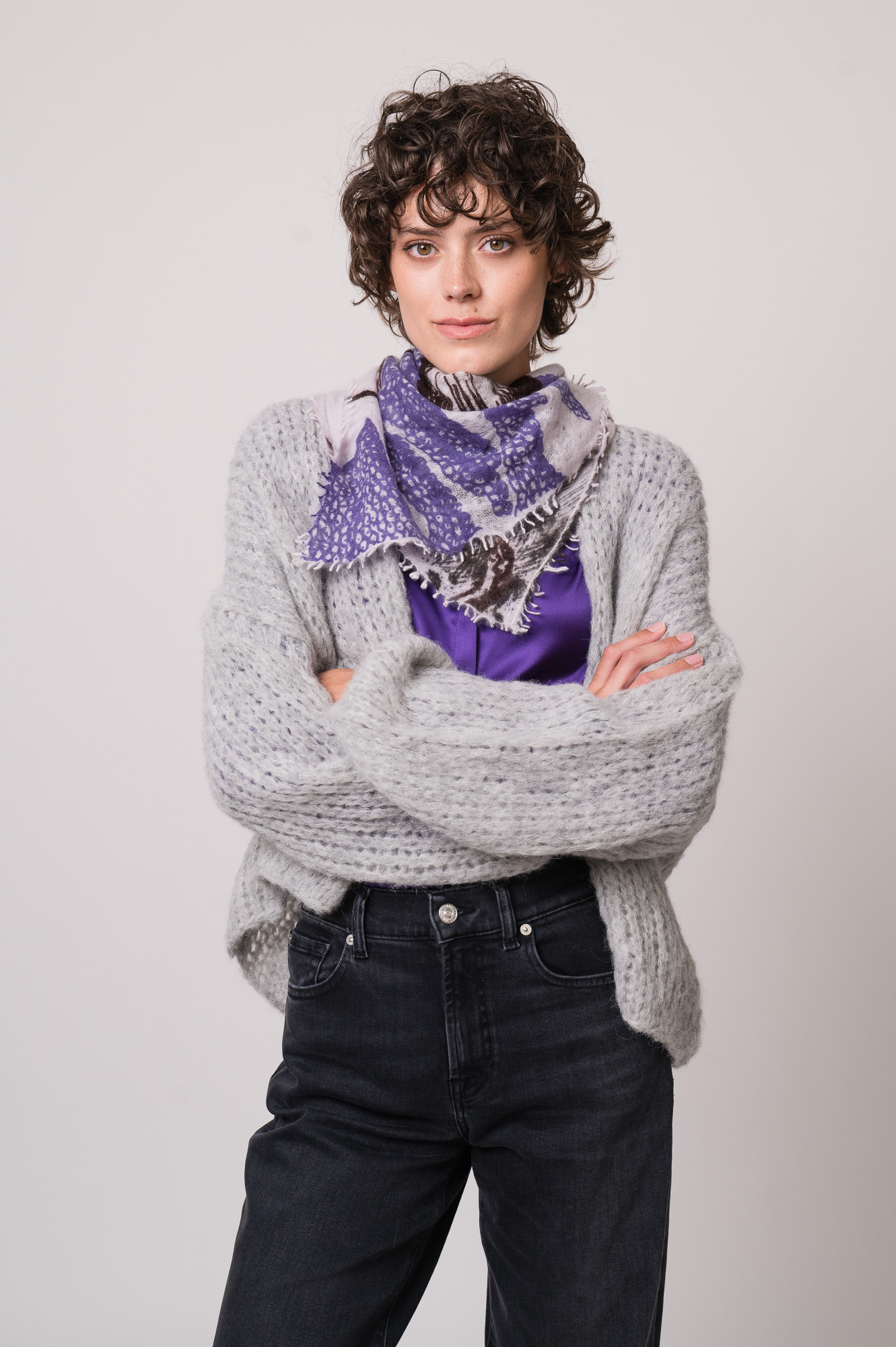 Model trägt eine graue Weste der Marke Michele & Hoven, eine violette Bluse der Marke Herzens und eine schwarze Jeans der Marke 7 for all mankind und ein Tuch von Mouleta.
