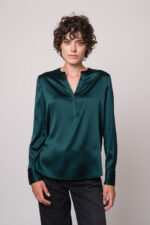 Model trägt eine grüne Bluse der Marke Herzens und eine schwarze Jeans der Marke 7 for all mankind.
