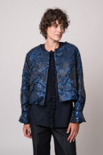 Model trägt eine marine-blaue Jacke mit Metallic-Effekt und eine marine-blaue Bluse der Marke Susanne Bommer sowie eine Jeans der Marke Mason’s.