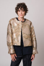 Model trägt eine goldene Jacke mit Metallic-Effekt und eine marine-blaue Bluse der Marke Susanne Bommer