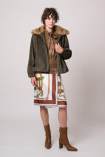 Model trägt eine grüne Jacke des Marke Betta Corradi, einen braunen Kurzarmpullover, eine braune Bluse und einen gemusterten Rock der Marke Dorothee Schumacher.