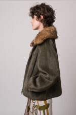Model trägt eine grüne Jacke des Marke Betta Corradi, einen braunen Kurzarmpullover, eine braune Bluse und einen gemusterten Rock der Marke Dorothee Schumacher.
