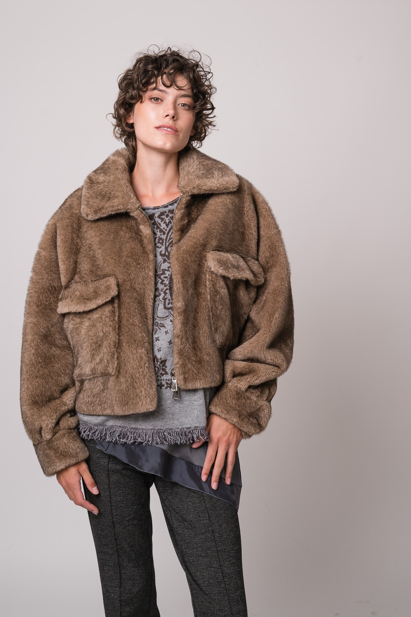 Model trägt eine braune Fake Fur Jacke der Marke Betta Corradi, ein graues Seidentop der Marke Luisa Cerano, einen grau gemusterten Pullover der Marke Grace.