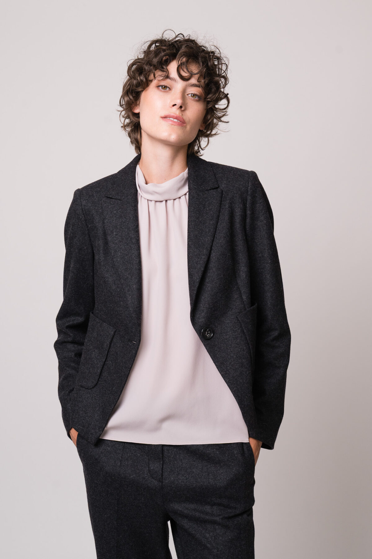 Model trägt eine helle Bluse, einen grauen Blazer und eine graue Hose der Marke Luisa Cerano.
