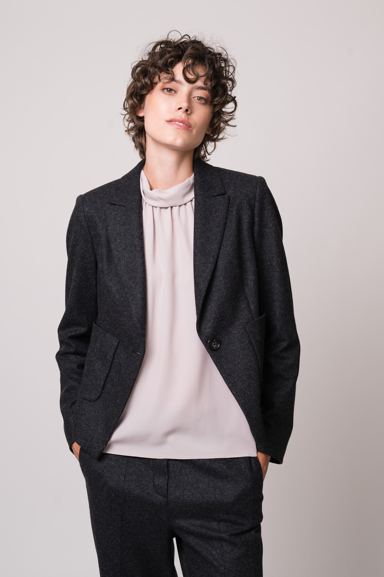 Model trägt eine helle Bluse, einen grauen Blazer und eine graue Hose der Marke Luisa Cerano.
