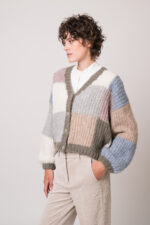 Model trägt eine weiße Bluse der Marke SOSU und eine bunte Strickweste der Marke Michele & Hoven.