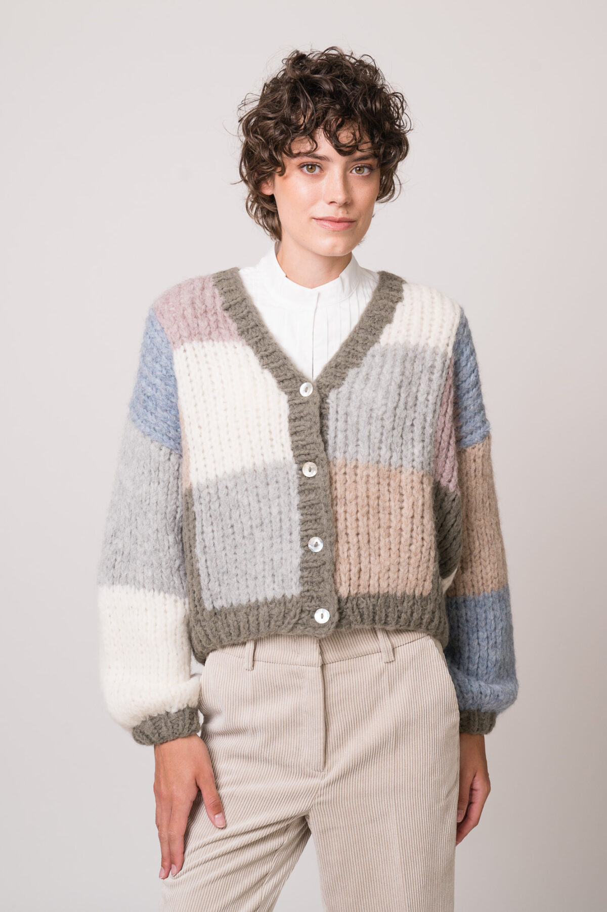 Model trägt eine weiße Bluse der Marke SOSU und eine bunte Strickweste der Marke Michele & Hoven.