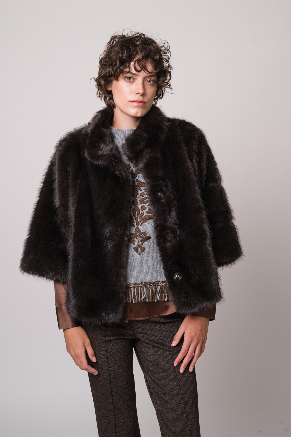 Model trägt eine braune Bluse der Marke The Mercer, einen hellgrau gemusterten Pullunder der Marke Grace sowie eine dunkelbraune Fake Fur Jacke der Marke Luisa Cerano.