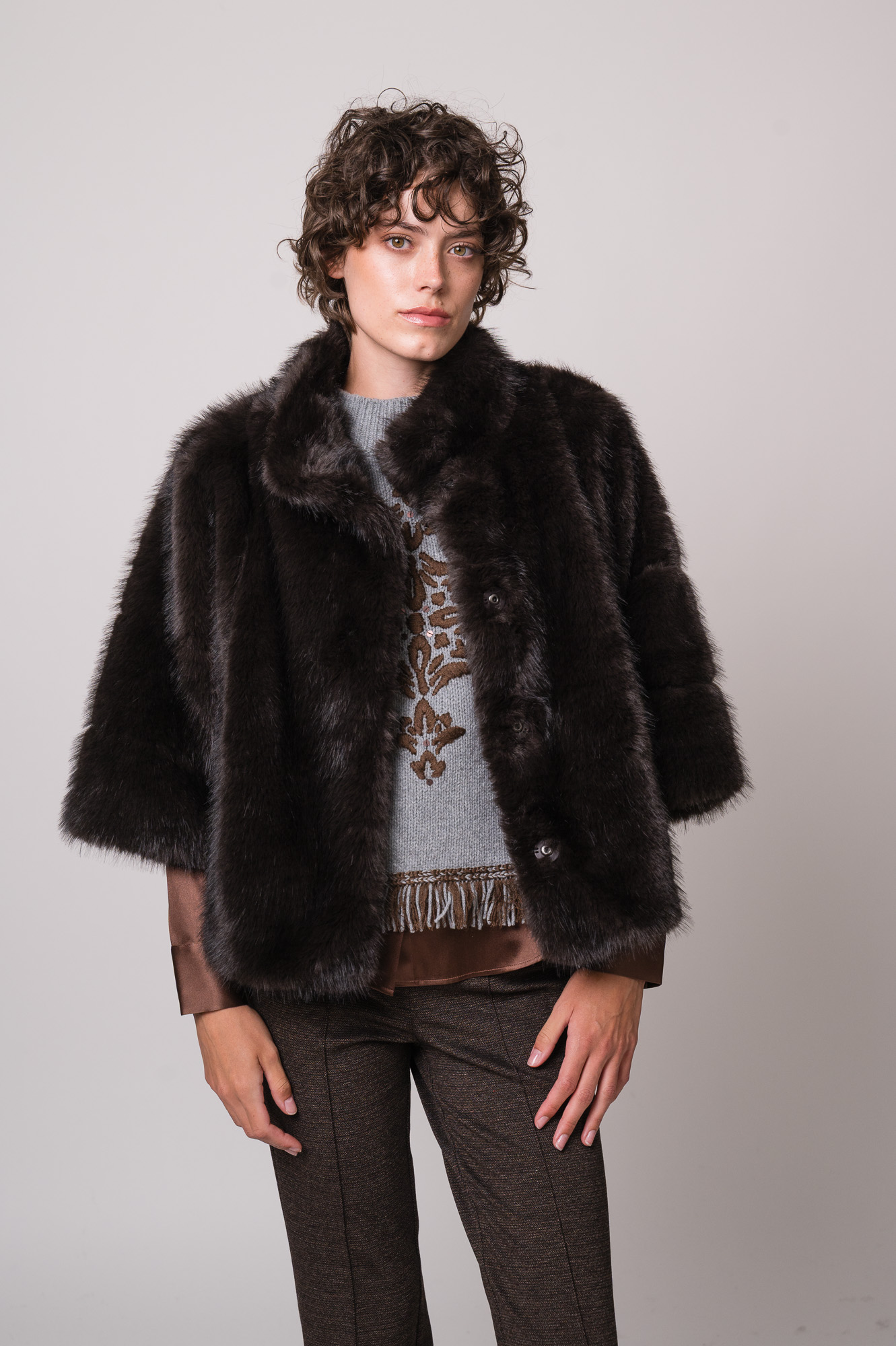 Model trägt eine braune Bluse der Marke The Mercer, einen hellgrau gemusterten Pullunder der Marke Grace sowie eine dunkelbraune Fake Fur Jacke der Marke Luisa Cerano.
