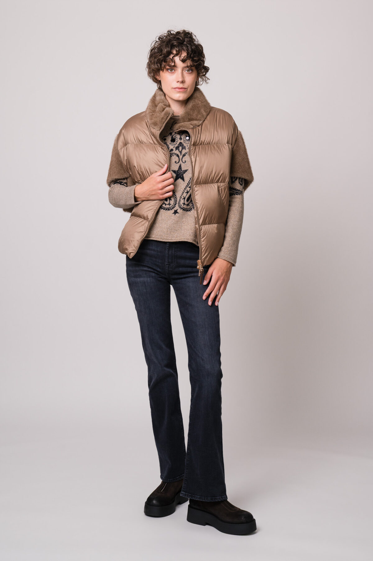 Model trägt ein beiges Cape der Marke Mabrun und einen beige gemusterten Pullover der Marke Grace sowie eine Jeans der Marke 7 for all mankind.
