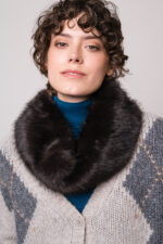 Model trägt eine grau gemusterte Weste und einen türkisfarbigen Rollkragenpullover sowie einen Fake Fur Schlauchschal der Marke Luisa Cerano.