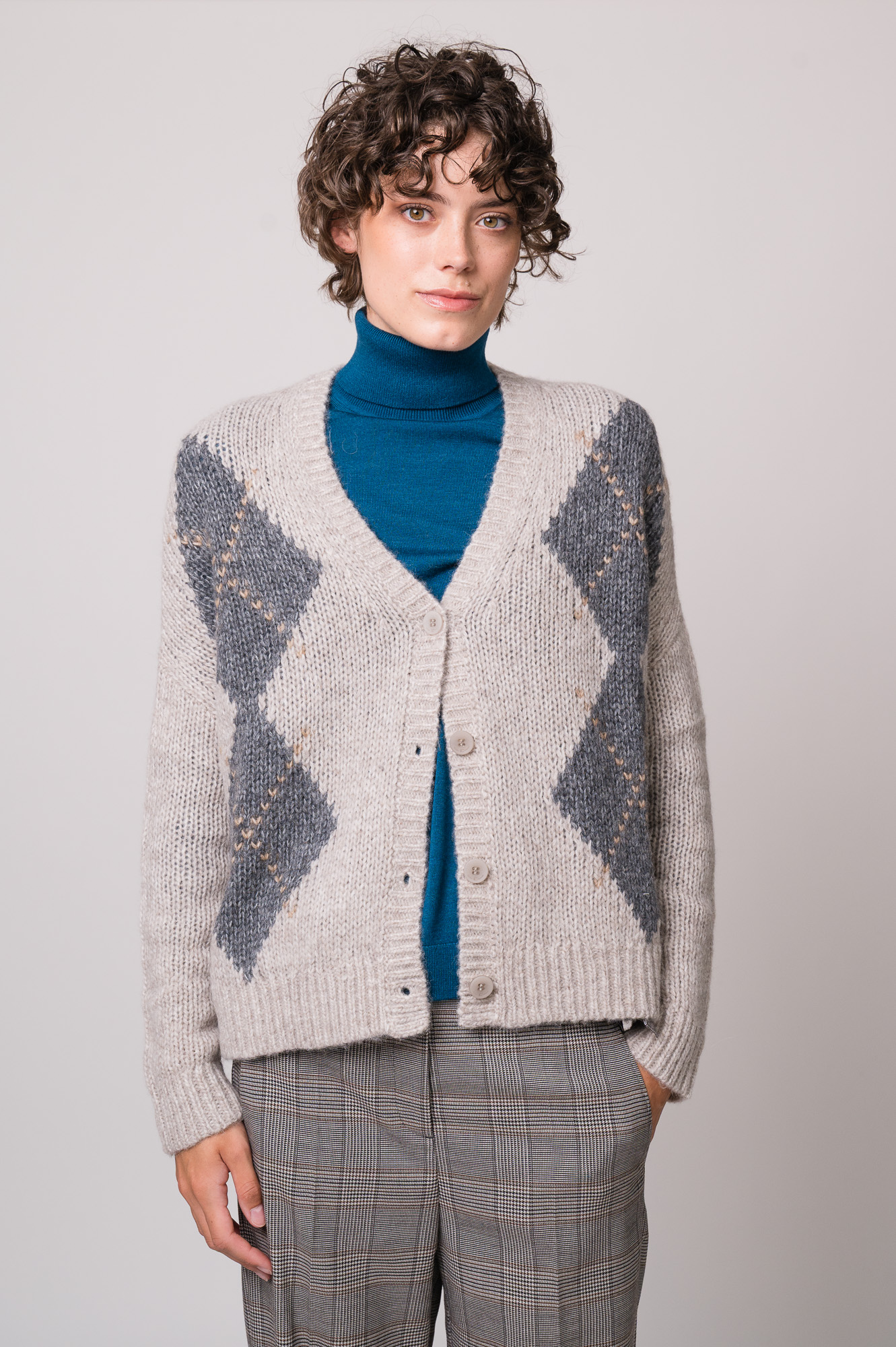 Model trägt eine grau gemusterte Weste und einen türkisfarbigen Rollkragenpullover der Marke Luisa Cerano.