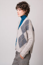 Model trägt eine grau gemusterte Weste und einen türkisfarbigen Rollkragenpullover der Marke Luisa Cerano.
