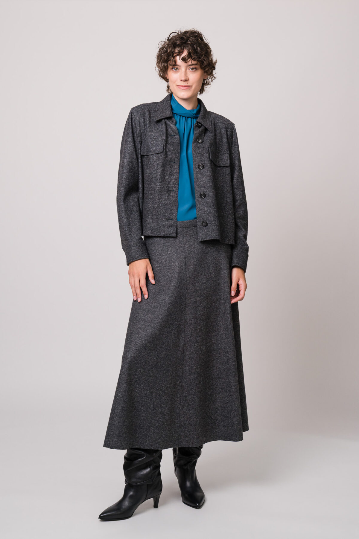 Model trägt eine graue Blazerjacke und einen grauen Rock sowie eine türkisblaue Bluse der Marke Luisa Cerano.