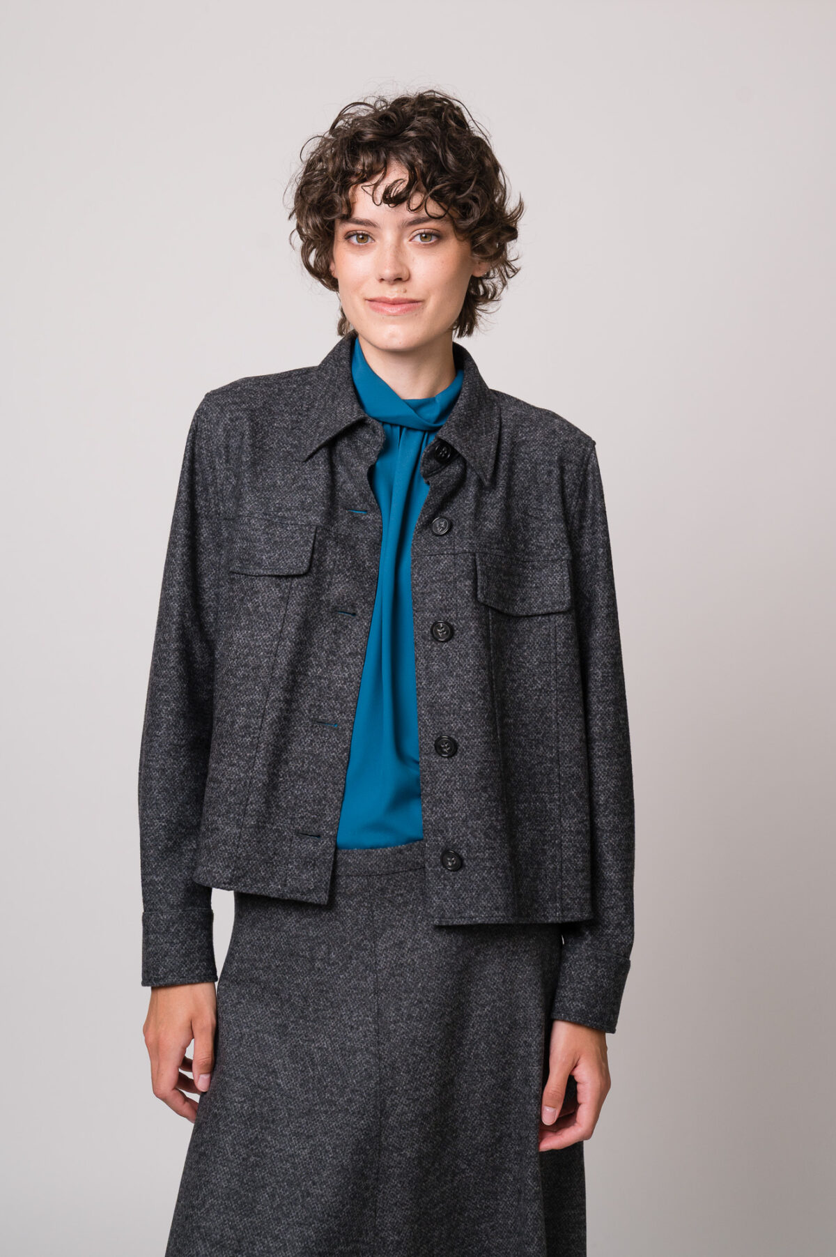 Model trägt eine graue Blazerjacke und eine türkisblaue Bluse der Marke Luisa Cerano.