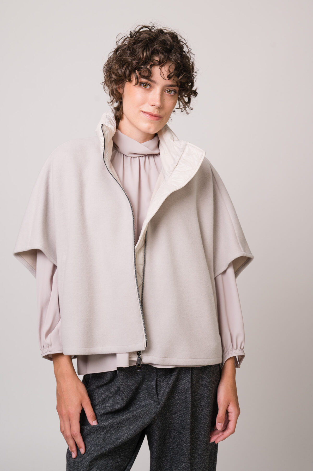 Model trägt ein naturfarbiges Cape und Bluse von Luisa Cerano.