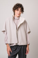 Model trägt ein naturfarbiges Cape und Bluse von Luisa Cerano.